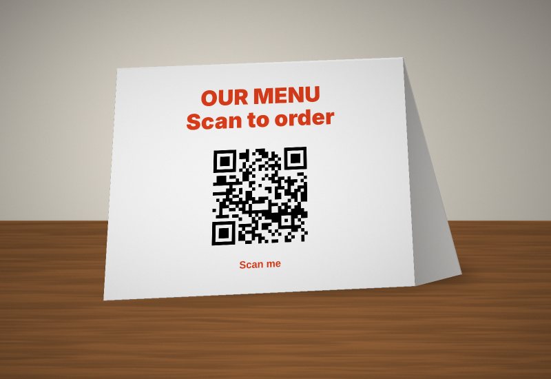 Printed NERGtags paper table tent reading OUR MENU, Scan to order, with a QR code, standing on a wooden table